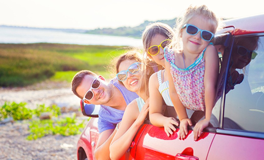 Ratgeber Urlaub mit dem Auto - Vierköpfige Familie guckt fröhlich aus dem Auto